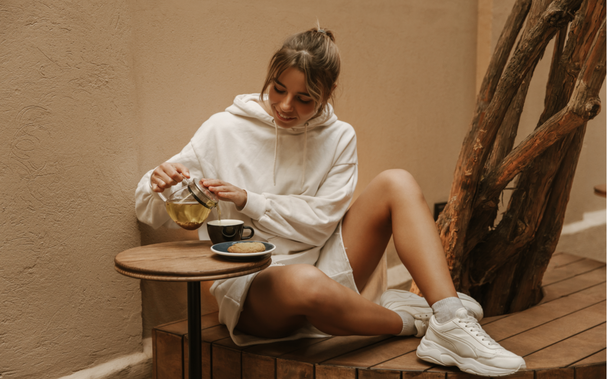 Blonde Frau in weißem Hoodie, kurze Hosen und Sportschuhe sitzt im Café