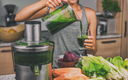 Frau entsaftet Gemüse in der Küche und macht green Juice
