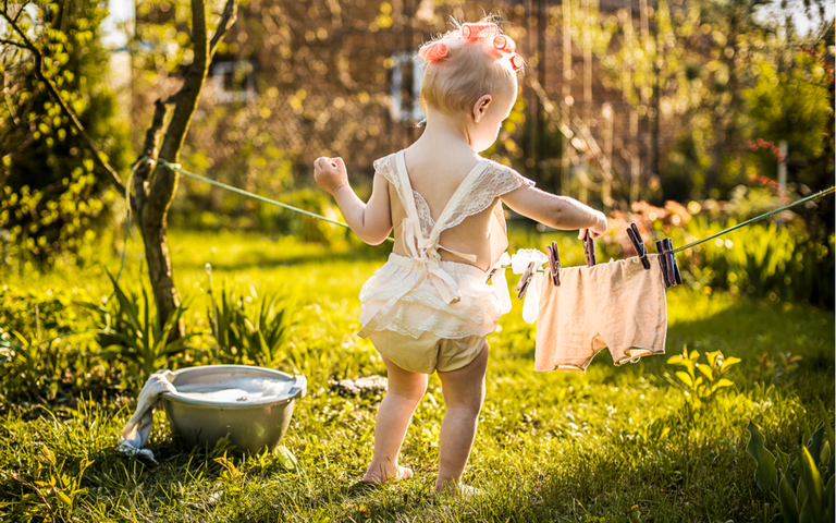 Baby hängt Wäsche auf im Garten