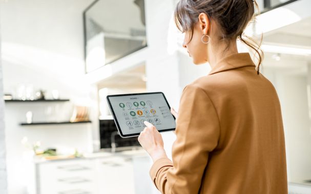 Frauen, die intelligente Heimgeräte mithilfe einer digitalen Tablette steuern, die im weißen Wohnzimmer eingesetzt wird. Smarthome-Konzept