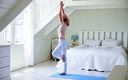 frau in yogapose steht im schlafzimmer und macht yoga mit fensterausblick