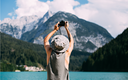 Junger Mann auf Bräune und Panama, der Fotos mit digitaler, spiegelloser Kamera des Alpensees mit blauem Wasser und Bergen macht.png