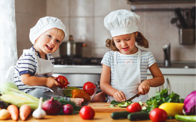 Zwei Kinder schneiden Gemüse auf in der Küche.png