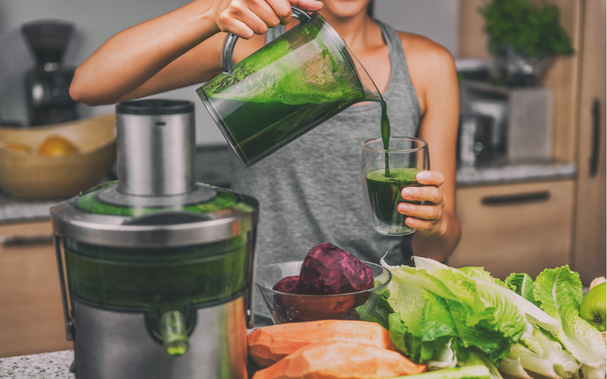 Frau entsaftet Gemüse in der Küche und macht green Juice