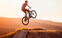 junger-mann-springt-mit-mountain-bike-auf-rampe-bei-sonnenuntergang