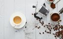 eine tasse kaffee gemahlener kaffee und ein aufgeschraubte espressokocher inlusive kaffeebohnen auf einem holztisch ausgestreut