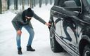 mann in mantel und mit haube kontrolliert den hinterreifen eines autos bei winterlichem wetter