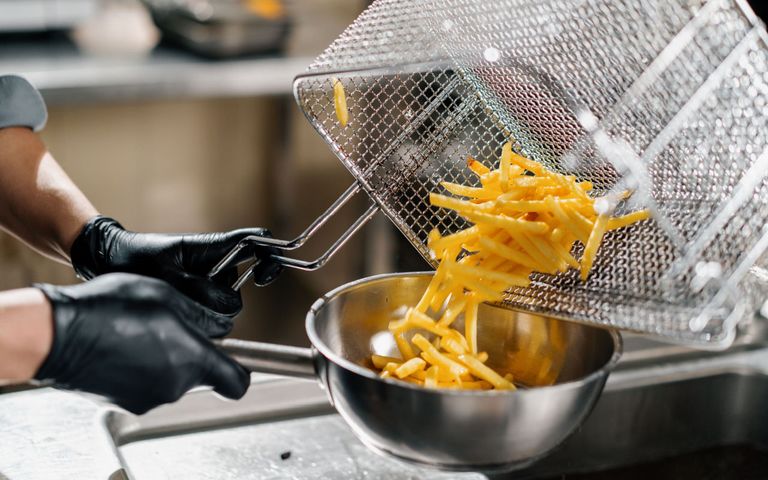 mensch-füllt-frittierte-pommes-aus-fritteuse-in-eine-metallschüssel