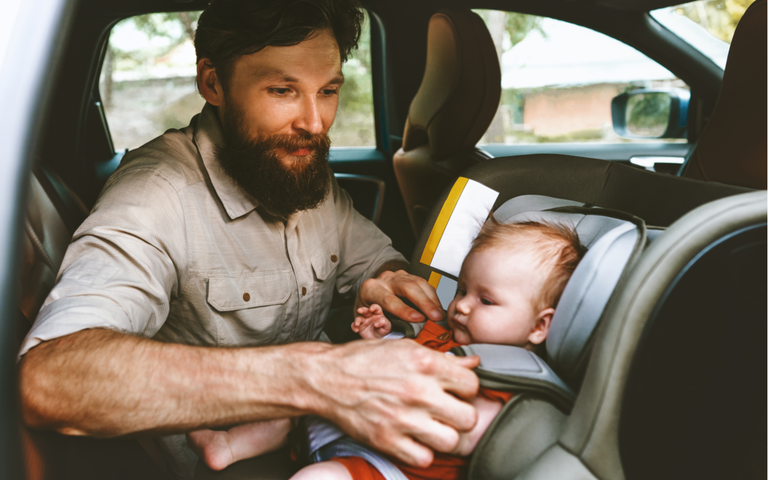 Vater sichert Baby im Autositz