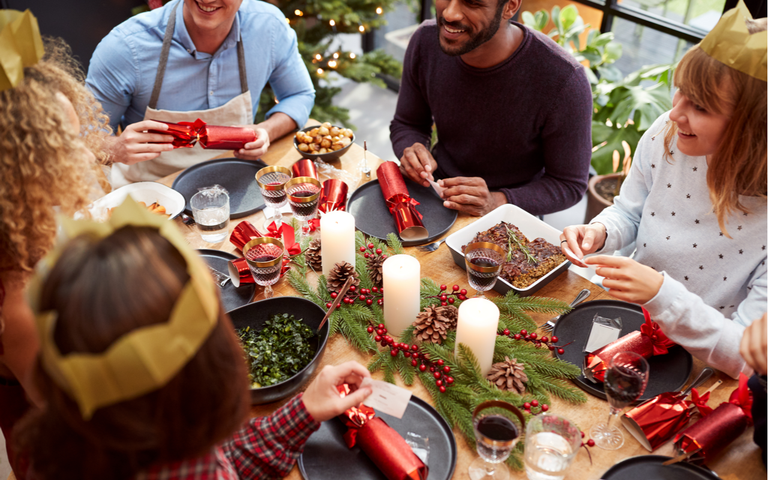 Junge Leute sitzen beim gedeckten Weihnachtstisch dekoriert mit Knallbonbons