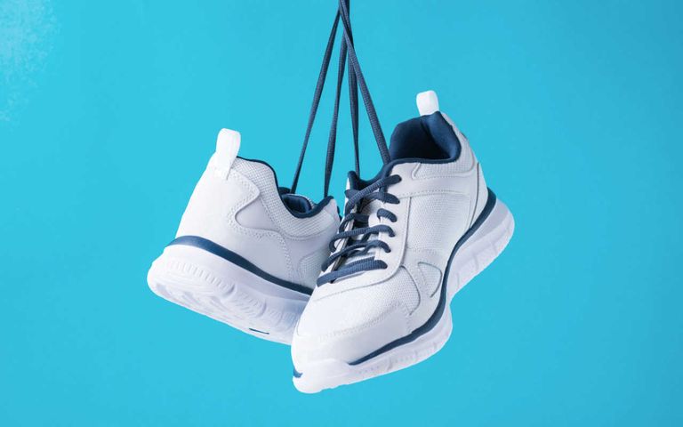 weiße-sneaker-hängen-an-schnürsenkeln-vor-blauen-hintergrund